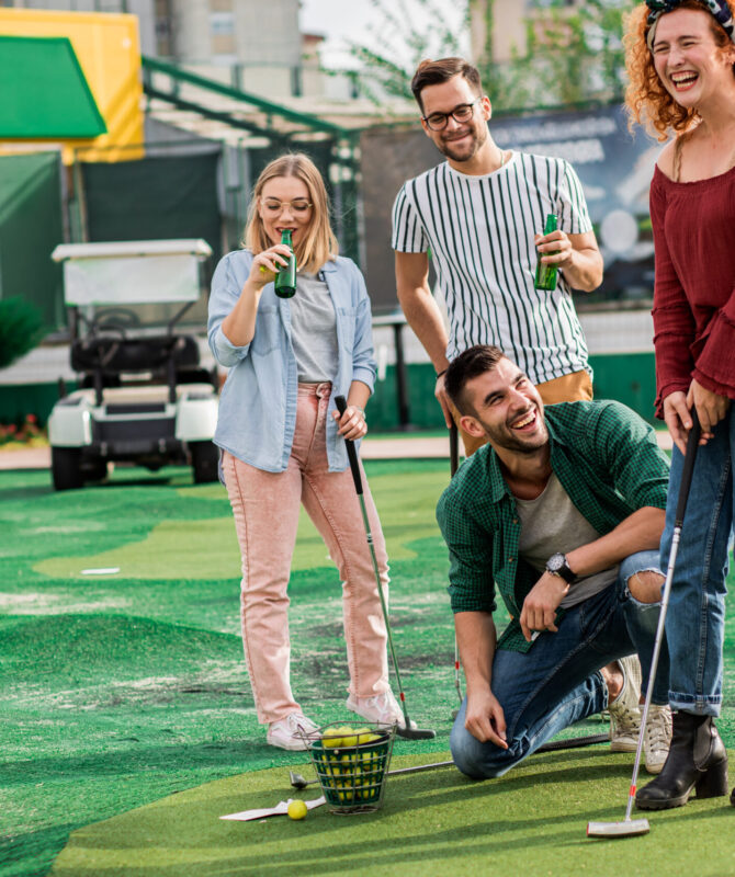 Group of smiling friends enjoying together playing mini golf in the city.