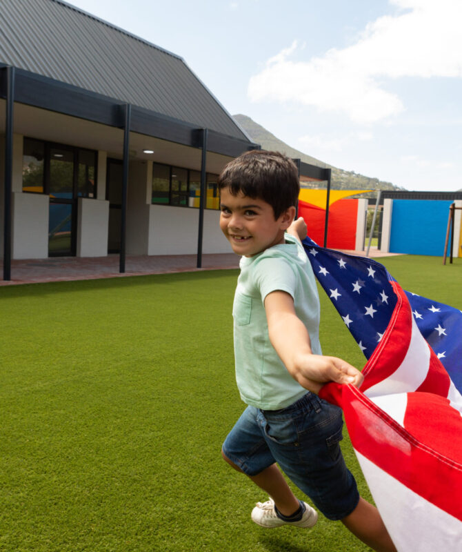 Side view of a Caucasian schoolboy running with an American flag in the school playground on a sunny day